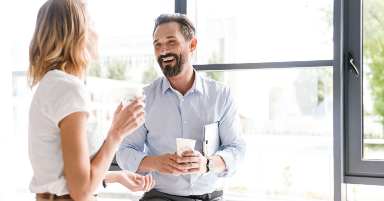 Happy colleagues talking while standing at the office window