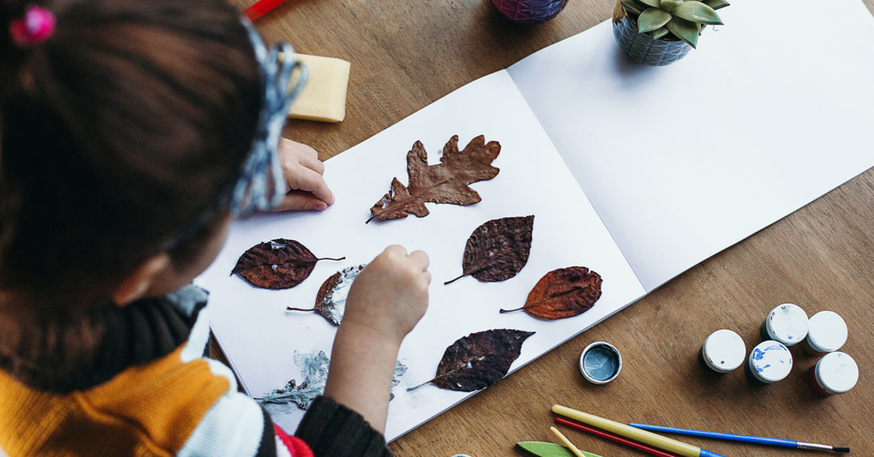 A child pastes dried leaves on a white album sheet