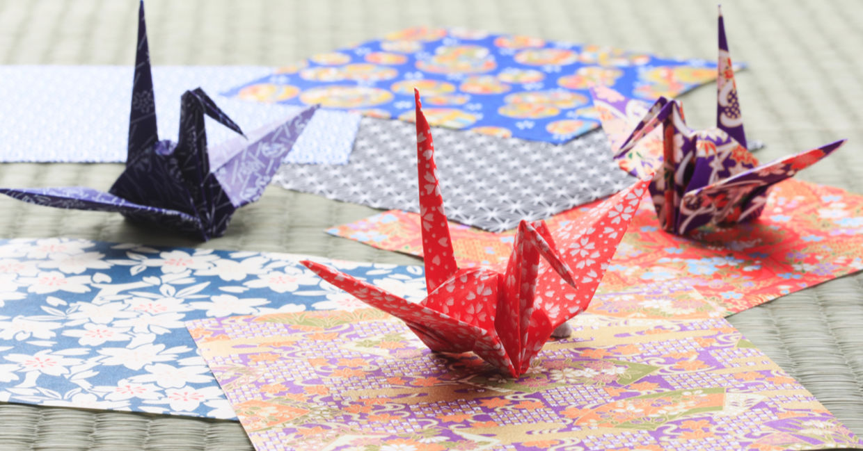 Origami paper cranes perch on colorful paper.