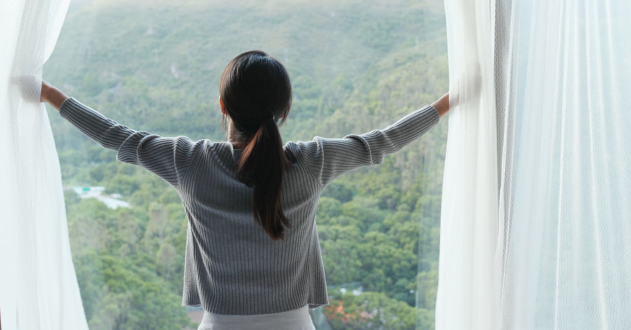 Woman opening a curtain to let in sunlight