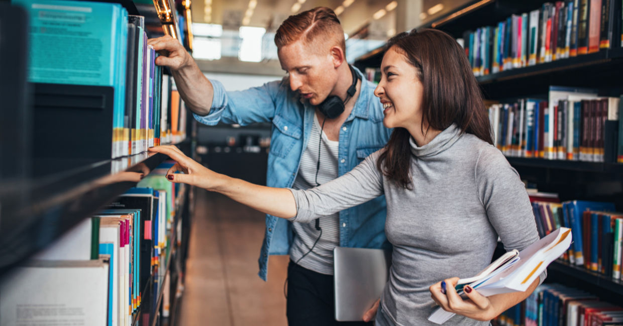 Two young students getting books from a public library shelf.