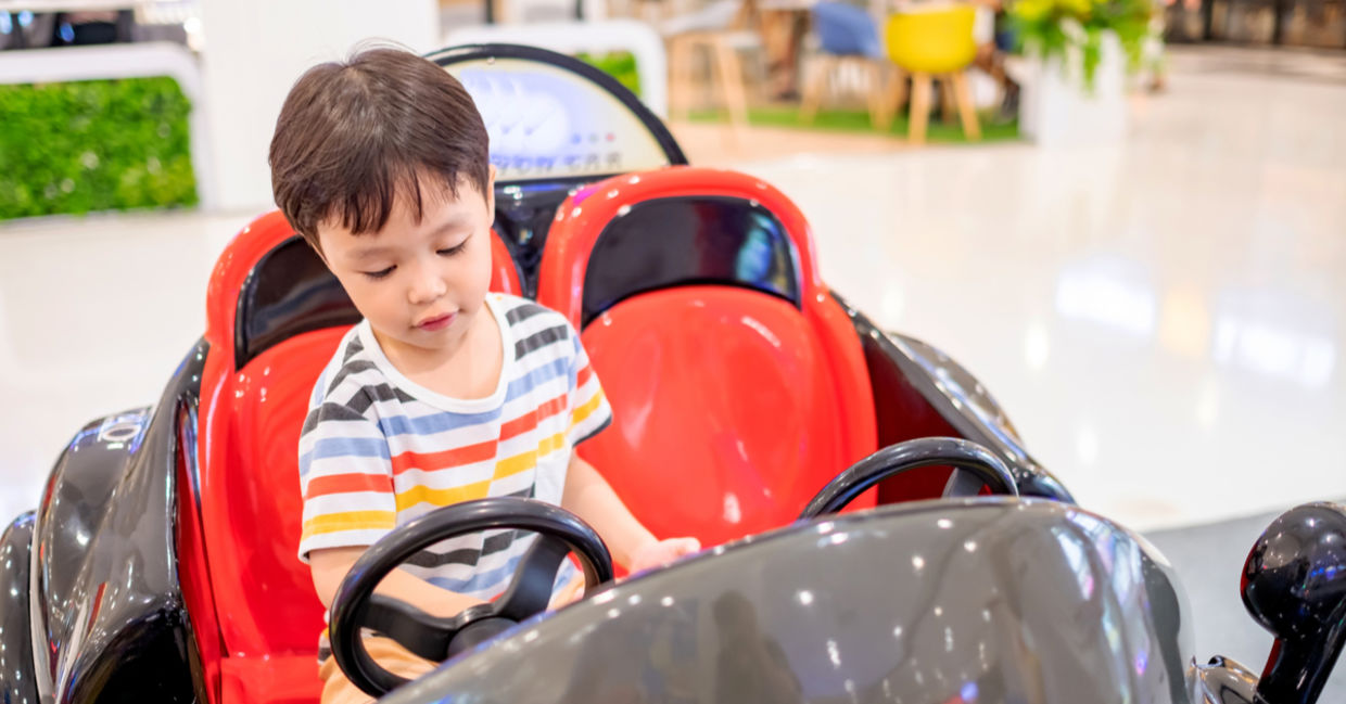 A young boy is riding in a coin-operated car.