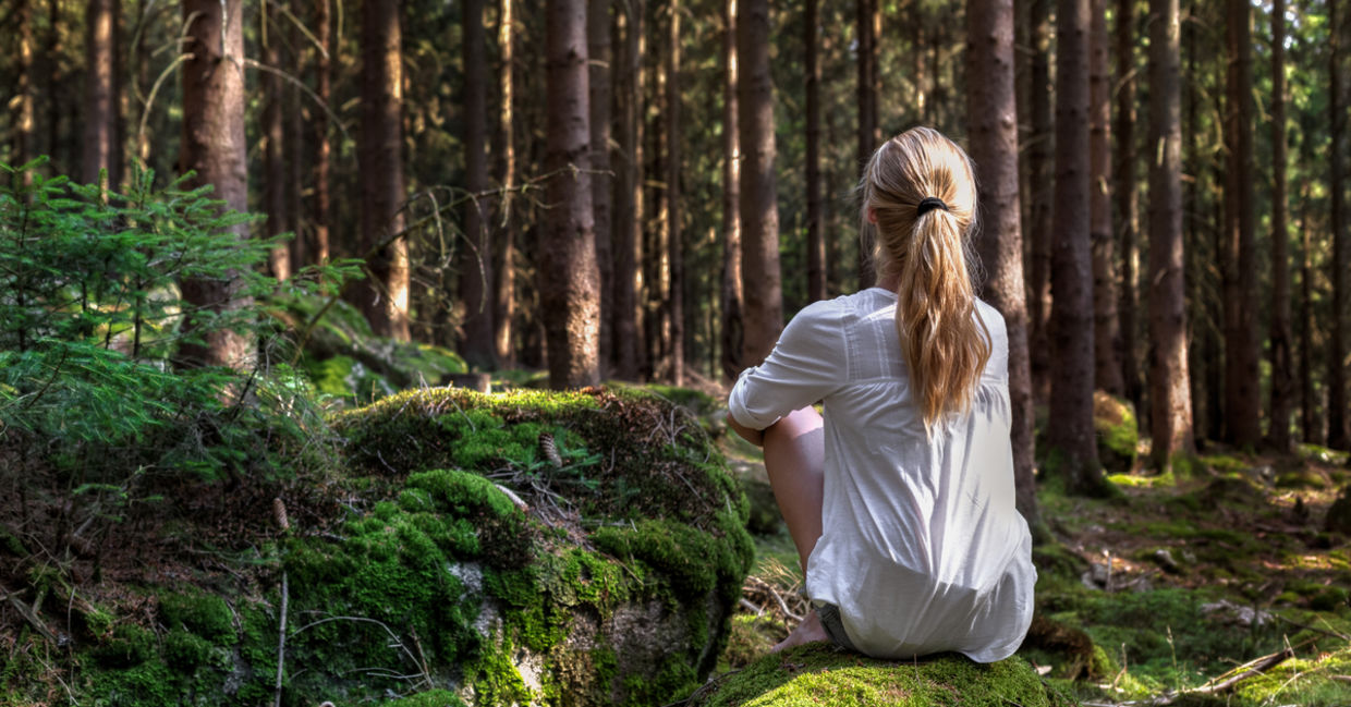 Woman sitting in green forest enjoys the silence and beauty of nature