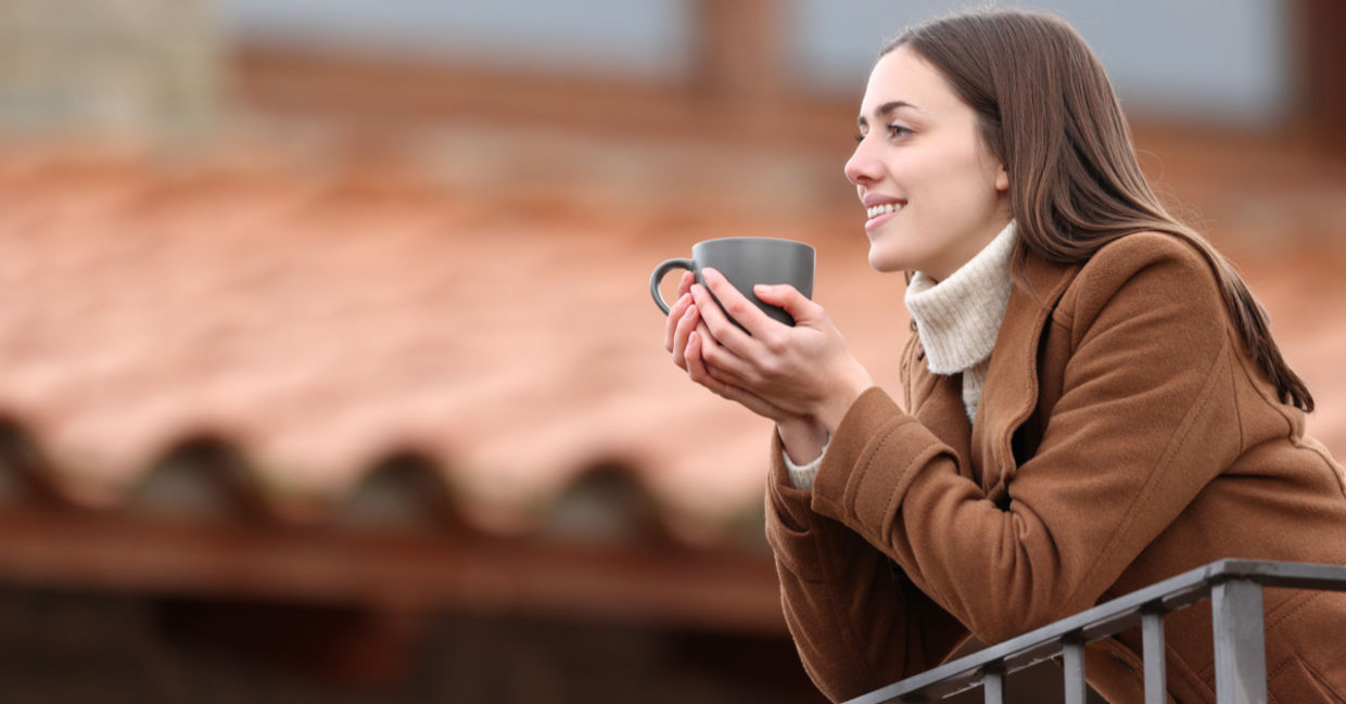Happy woman contemplating the view and drinking coffee on a balcony in winter