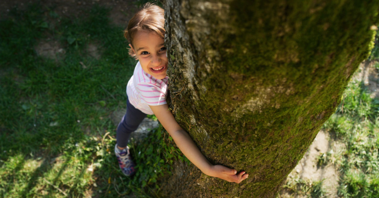 A happy little girl hugging a tree trunk