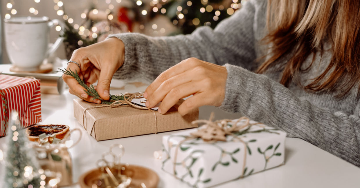 A woman sits in front of a Christmas and decorates her gifts with a sprig of juniper and DIY twine bows.