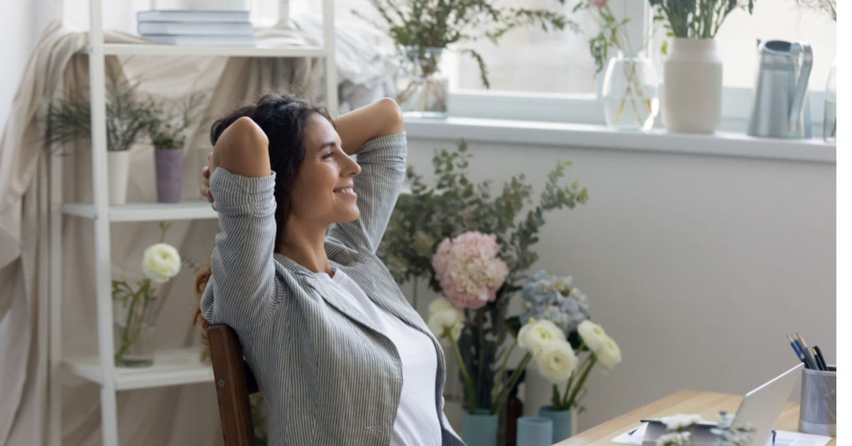 A woman feels calm and relaxed in her mindful workspace surrounded by flowers and soft colors.