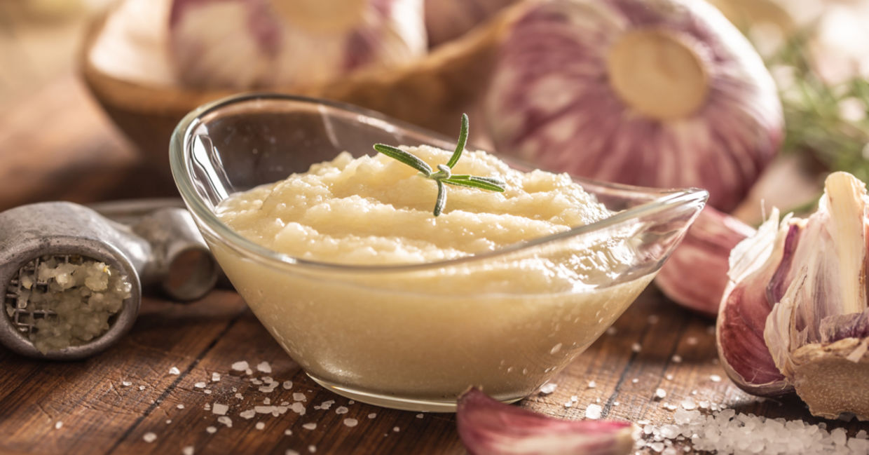 Garlic paste in a bowl with garlic cloves and sea salt.