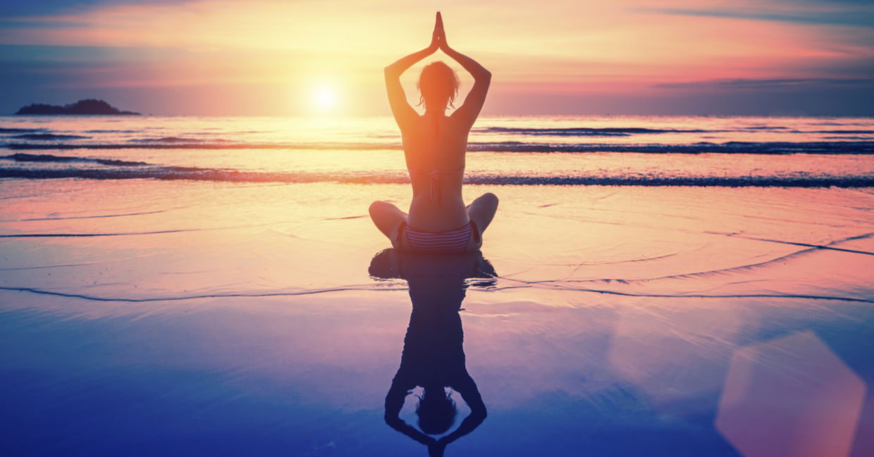 A woman meditates on the beach at sunset.