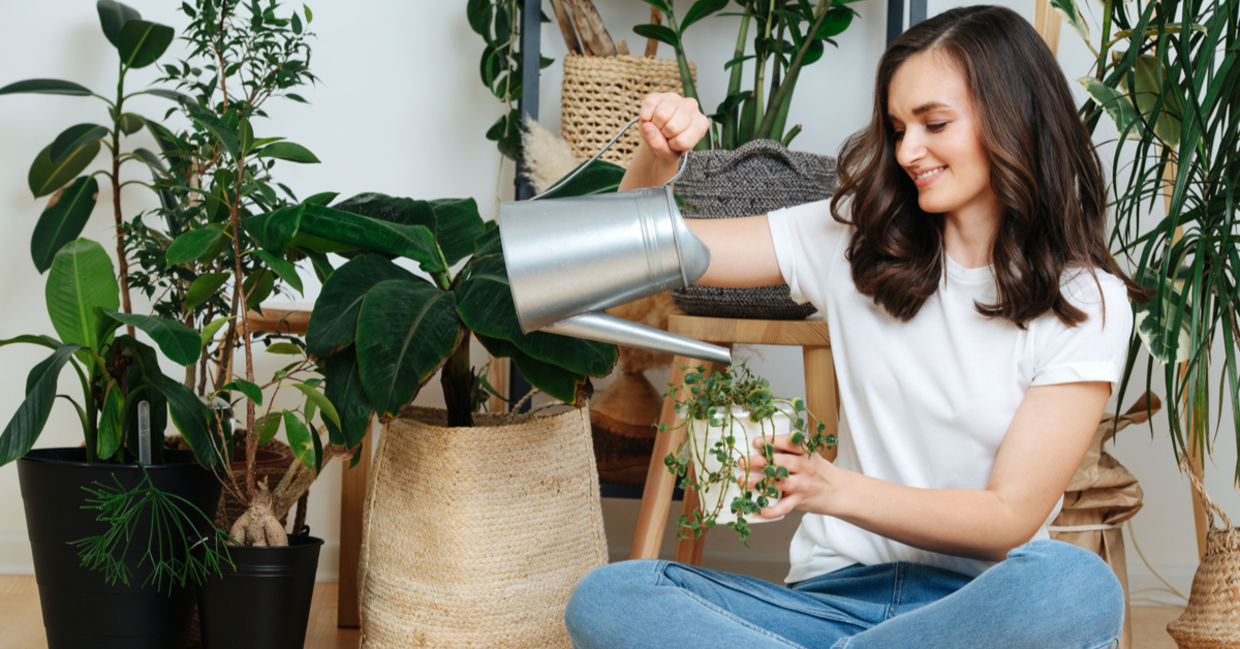 A woman sits on the floor caring for her houseplants.