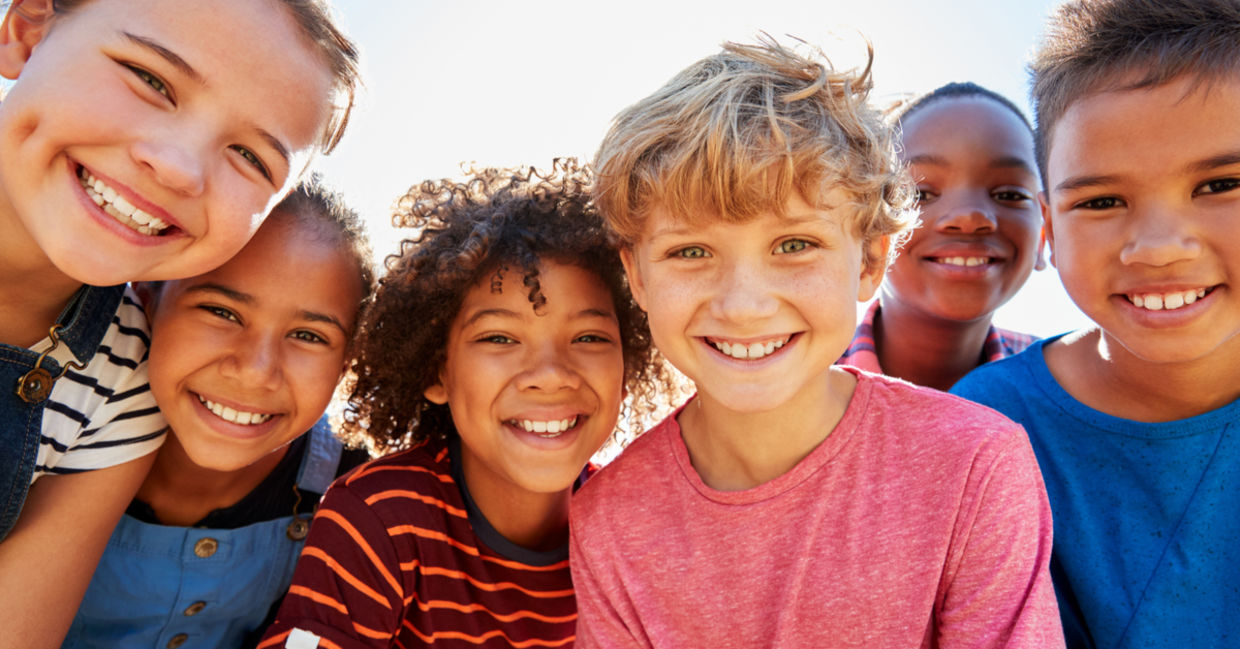 Close up of pre-teen friends in a park smiling to camera.