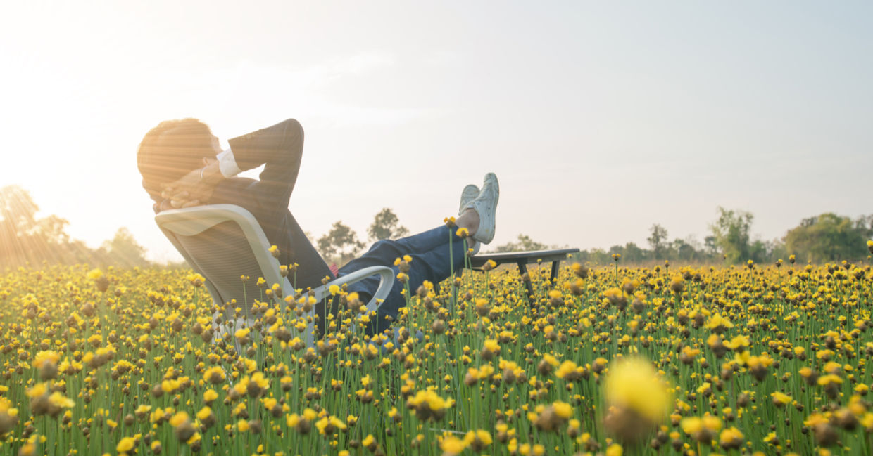 Businessman sitting in an office armchair and relaxing in a yellow flower field.