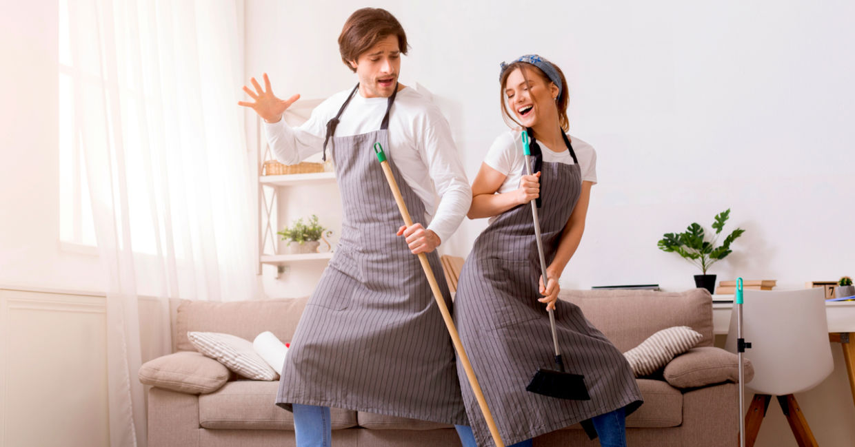 Cheerful couple having fun and dancing while spring cleaning their home.