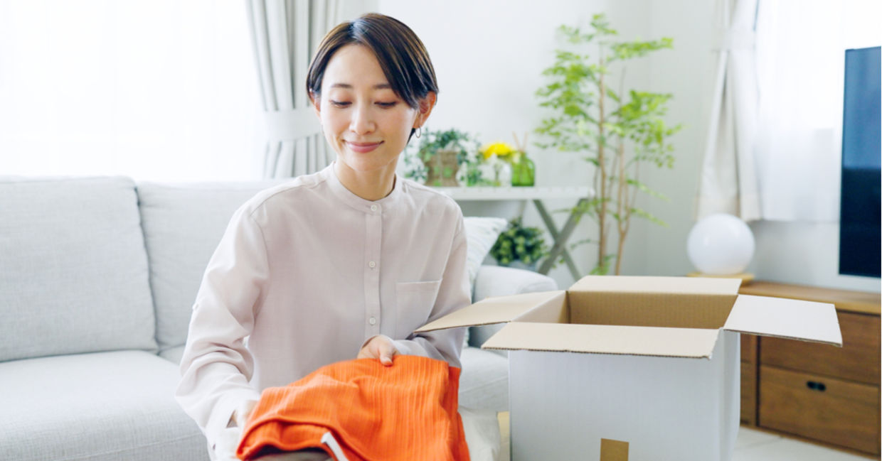 A woman stores seasonal clothes in a cardboard box.