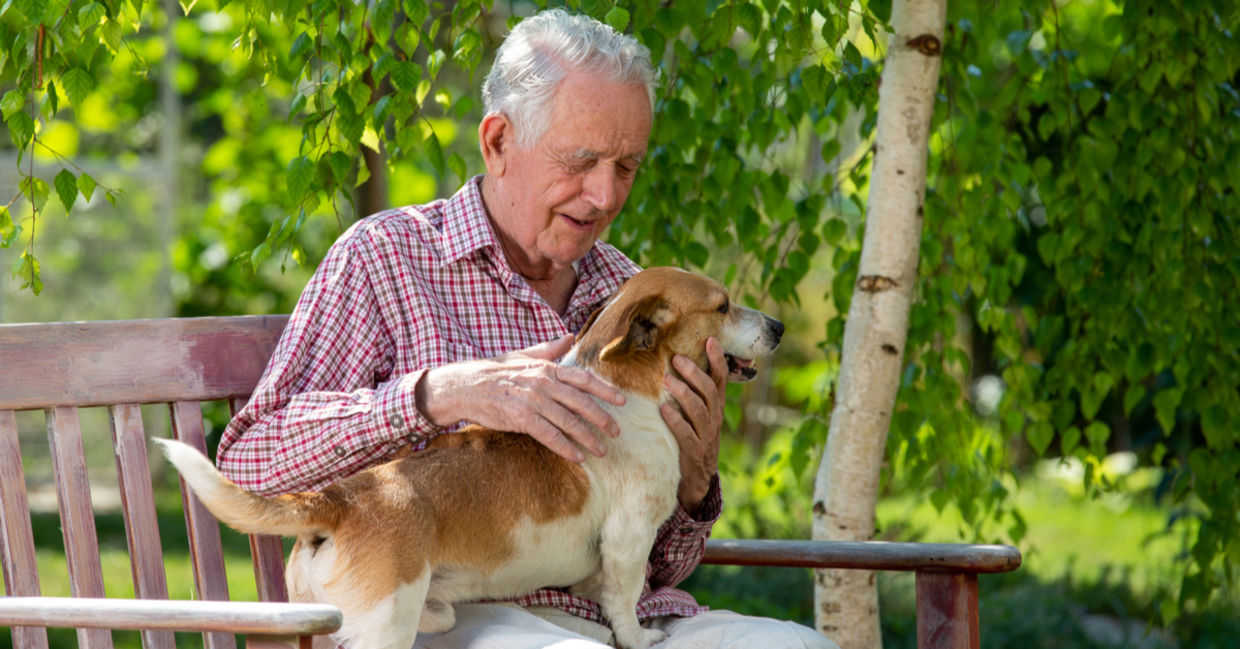 Senior man cuddling a dog outside.