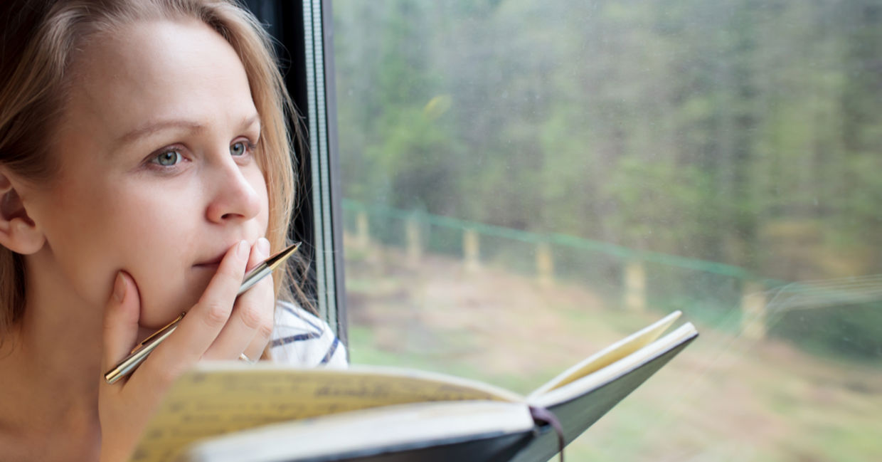 Woman on a train thinking about what to add to her journal.