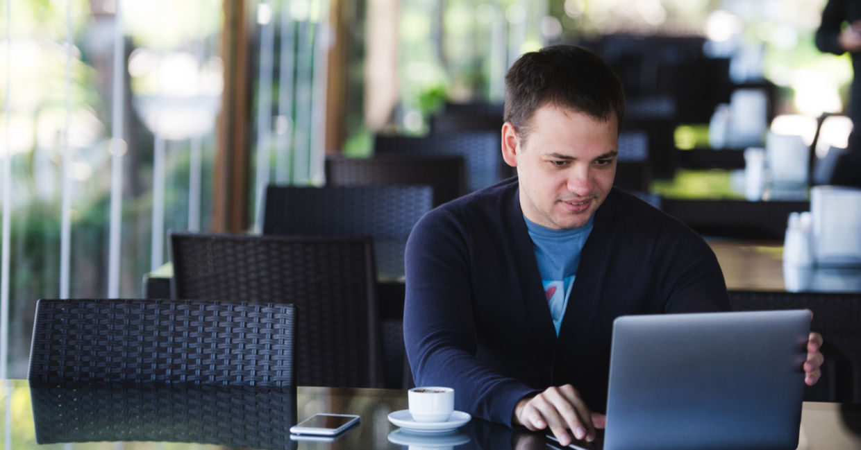 Concentrated male student studying with a laptop and drinking espresso.