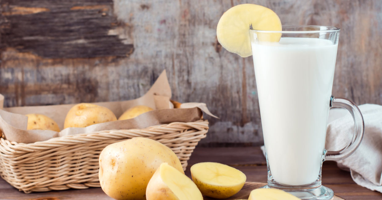 A glass of healthy potato milk is placed beside sustainable potatoes.