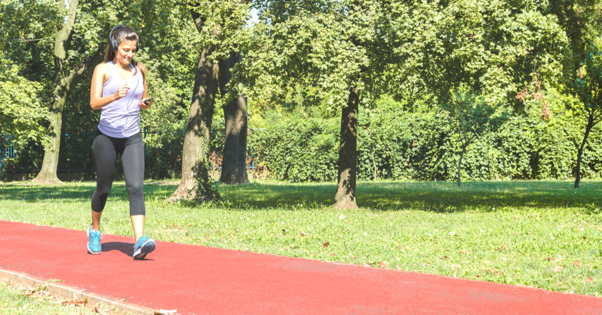 Woman walking briskly on a track listening to music.