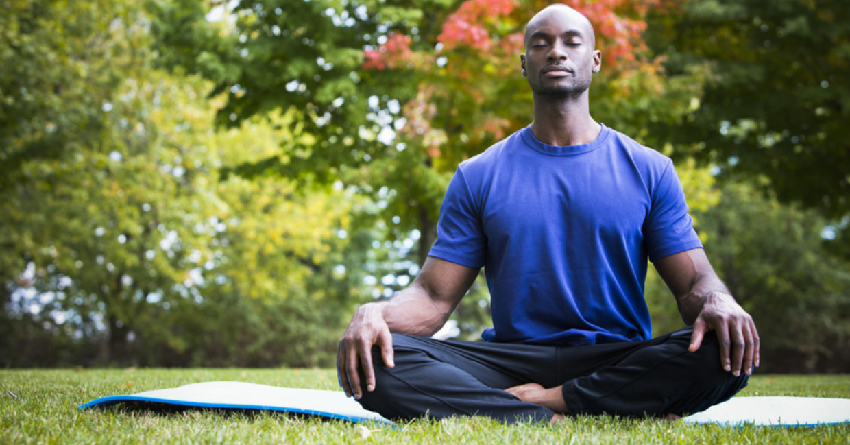 A man meditates outside on a yoga mat.