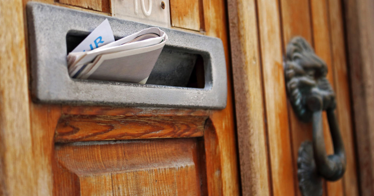 Mailbox filled with rolled spam newspaper in an old wooden door.