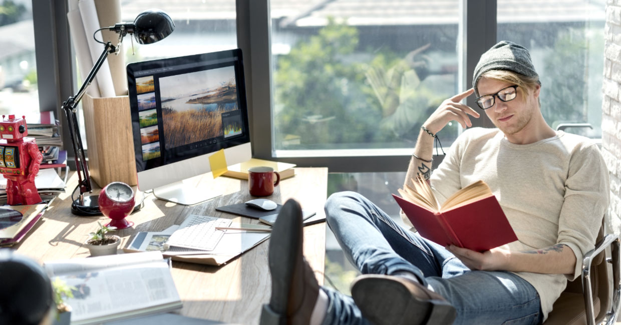 Man engrossed in reading a book at his workstation.