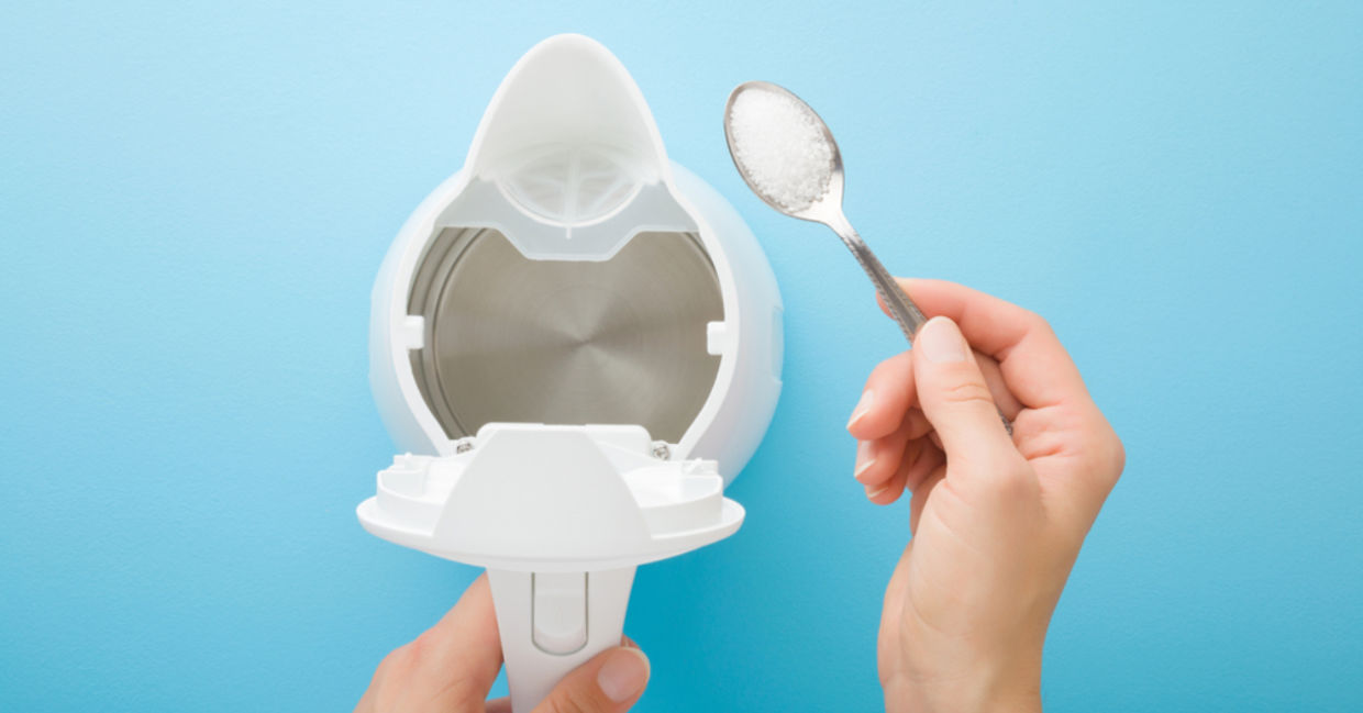 A woman holds a spoon of citric acid to descale a kettle.