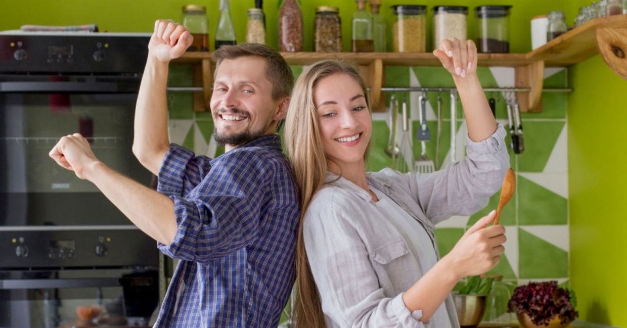 A couple cooks while they dance to music.