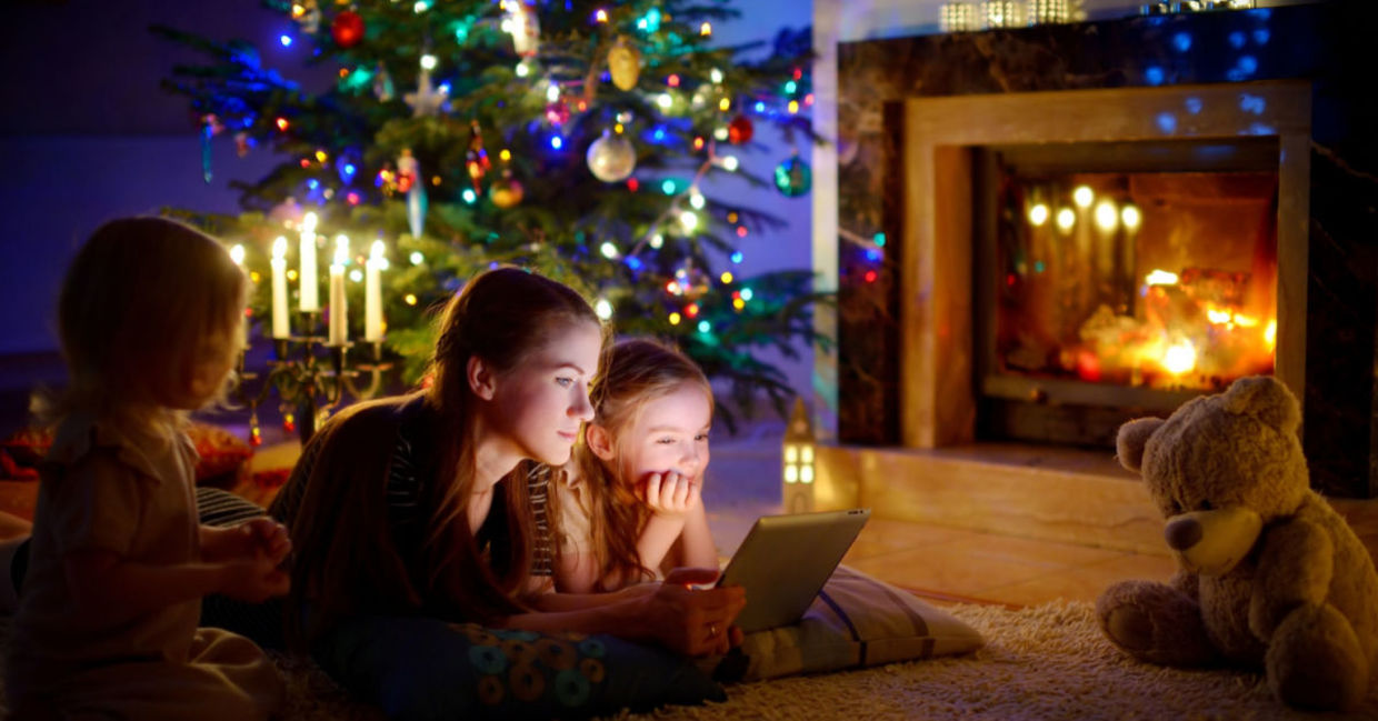 A young mom and her children watch a show at Christmas on a tablet.
