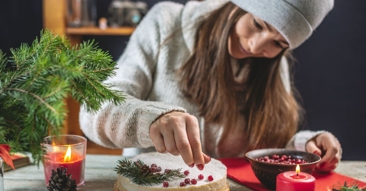 A woman decorating a festive cake with red berries.