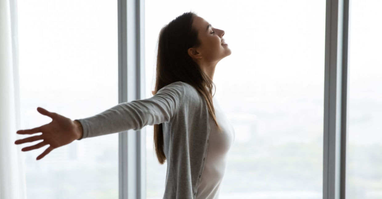A woman embraces life, smiling with arms wide open.