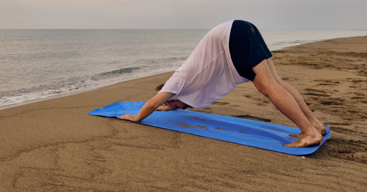 Doing the downward dog yoga pose at the beach.