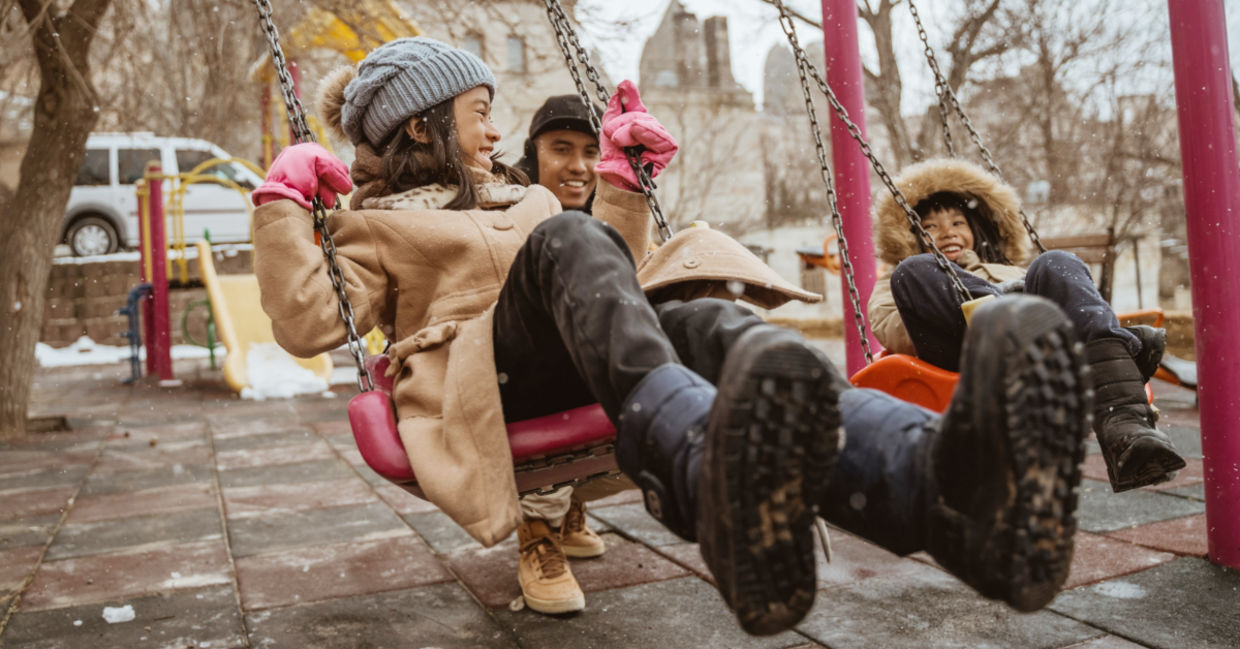 Father swinging his daughter in a playground during the winter.