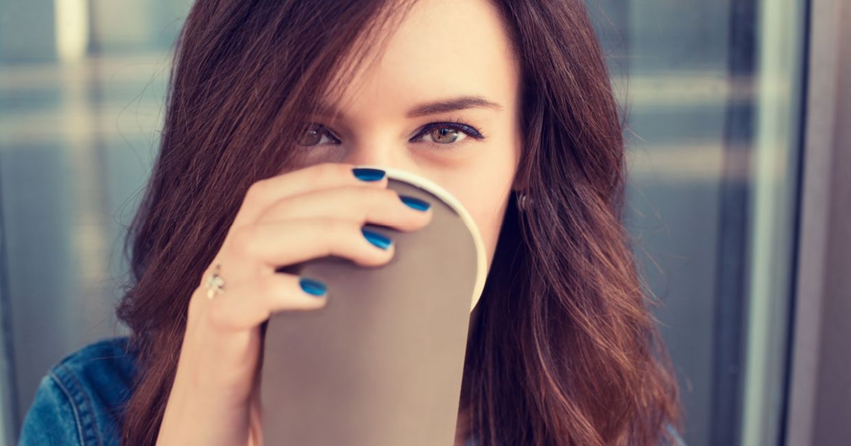 Smiling woman drinking coffee from a paper cup.