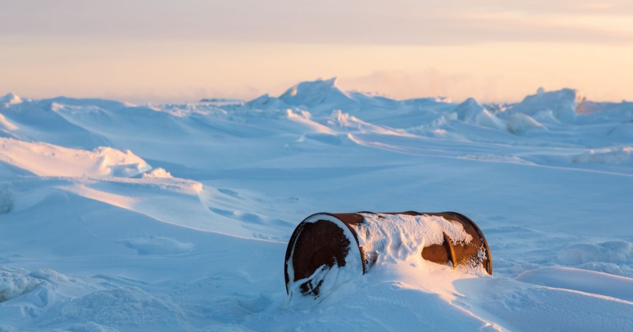 A rusty barrel on the shores of a frozen sea in the Arctic representing environmental pollution.