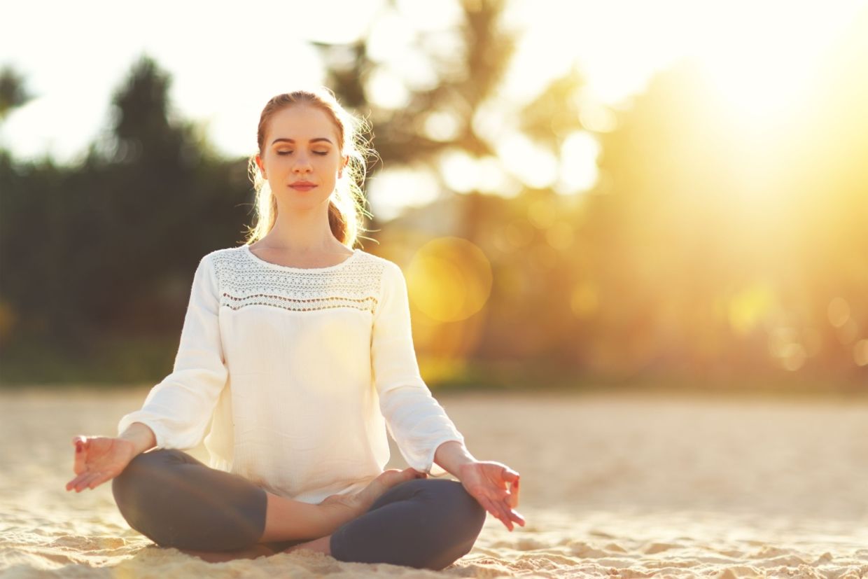 A woman practices yoga and meditates on the beach.