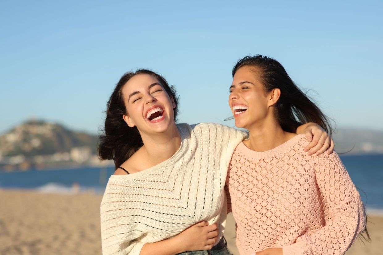 Two friends laugh while walking on the beach.