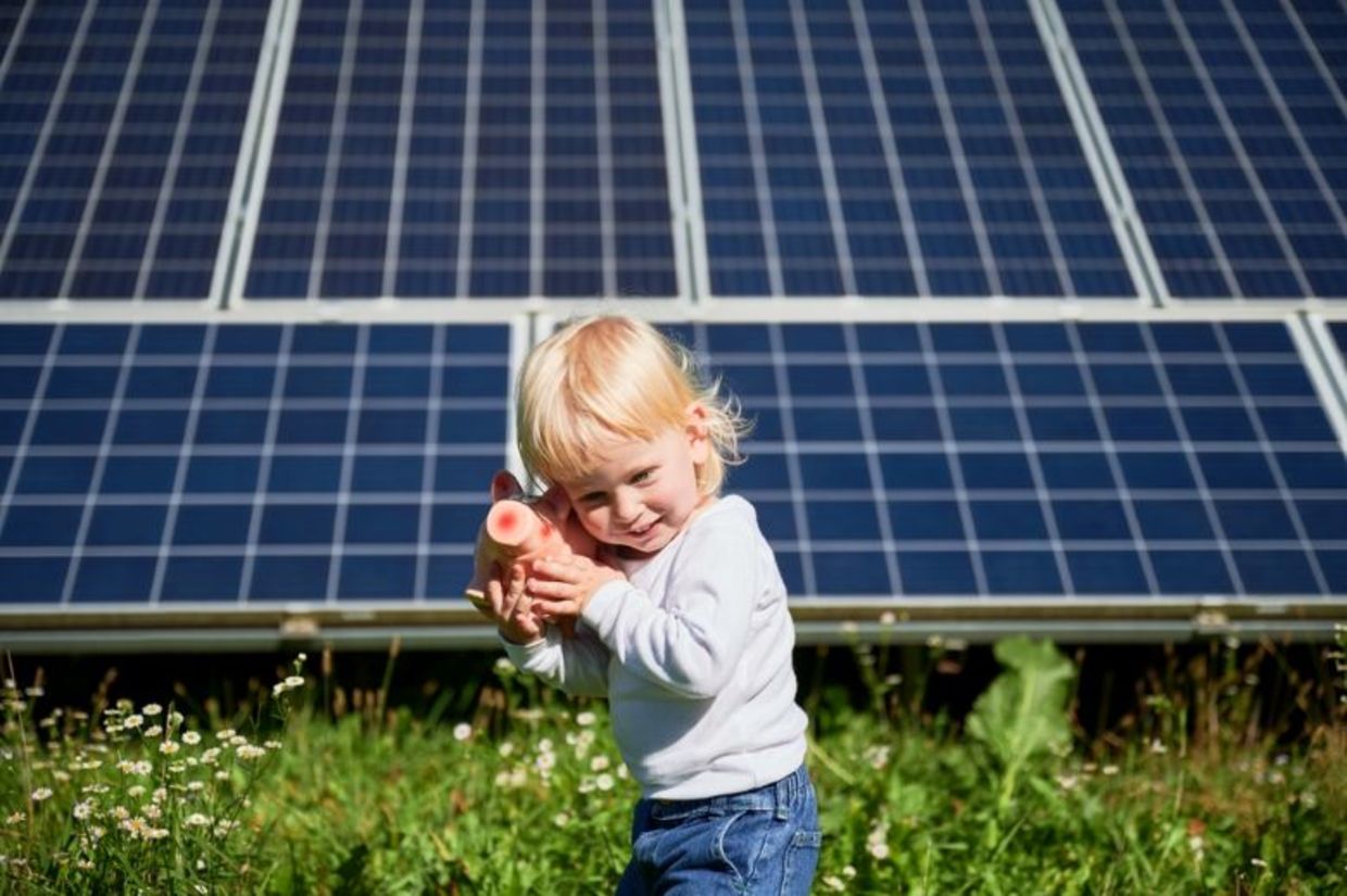 Child playing with a piggy bank in front of solar panels.