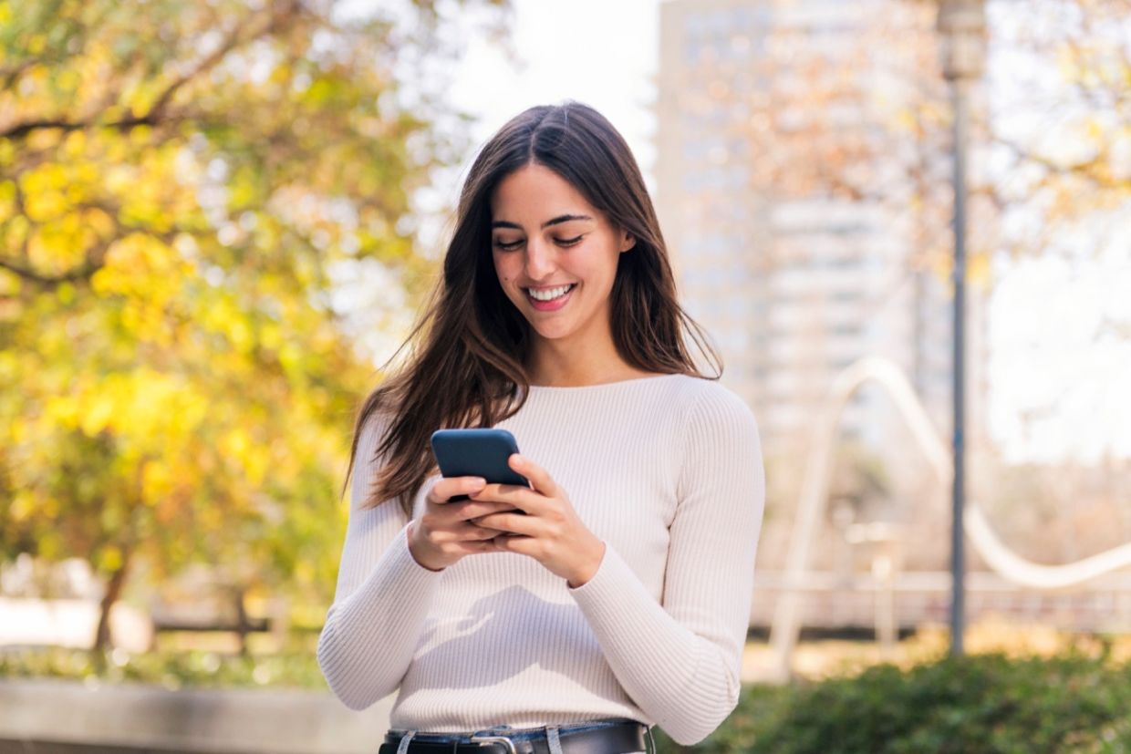 A woman smiles while she uses her phone.