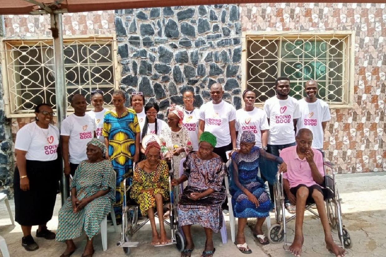 Good Deeds Day volunteers in Nigeria stand behind elderly residents seated outdoors.