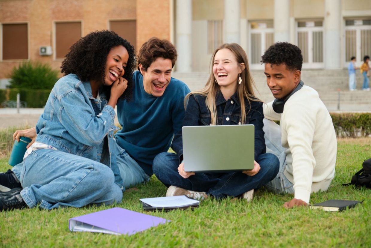 A diverse group of young adults sitting on the grass and smiling.