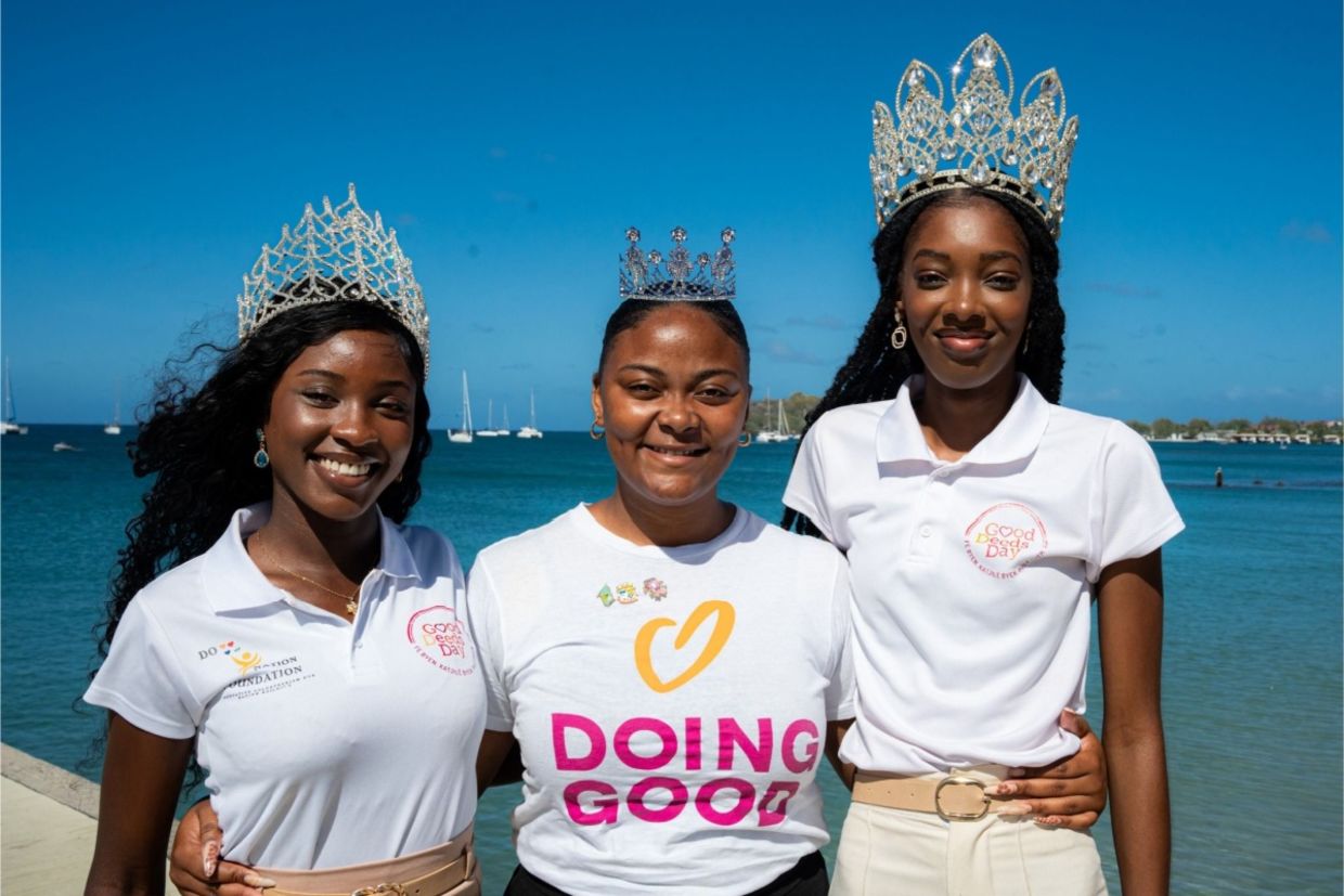 Three women wearing tiaras and Good Deeds Day shirts stand by the water.