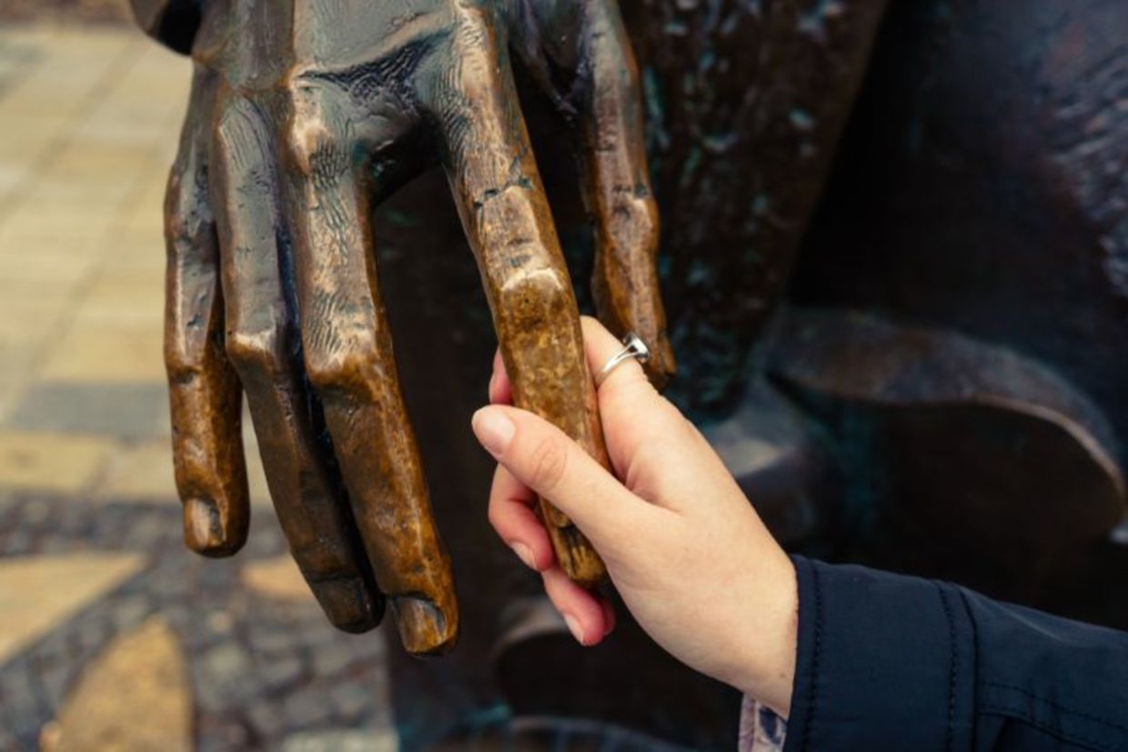 A visually impaired woman feels the hand of a bronze sculpture.